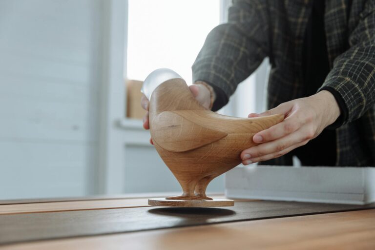Close-up of hands carefully holding a handmade wooden bird sculpture, showcasing artisan craftsmanship and design.